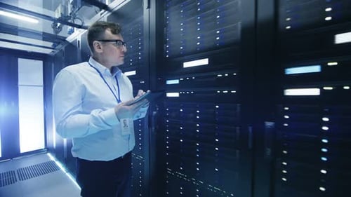 Following Shot of IT Engineer Walking Through Data Center Corridor with Rows of Rack Servers. He Us