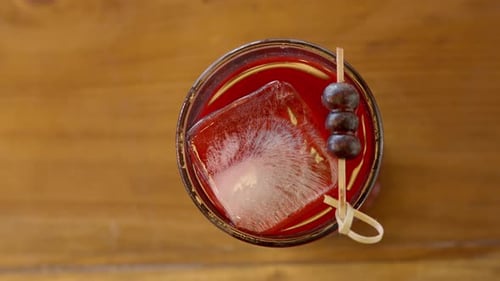 overhead video of a shot of berries with gin and blueberries served in a glass with ice cubes on a w