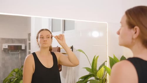 Woman Using Facial Massage Roller in Bathroom Mirror