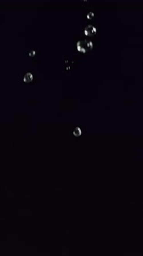 Wassertröpfchen in Zeitlupe, die elegant auf dunklen Hintergrund fallen