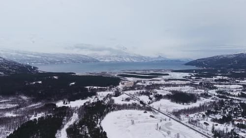 Aerial view of a snowy mountainous landscape with a lake and snowy forest in Norway