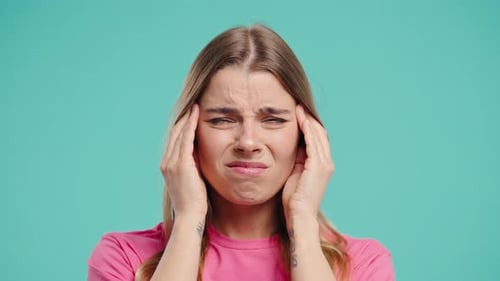 Woman Massaging Temples Experiencing Pain on a Teal Background