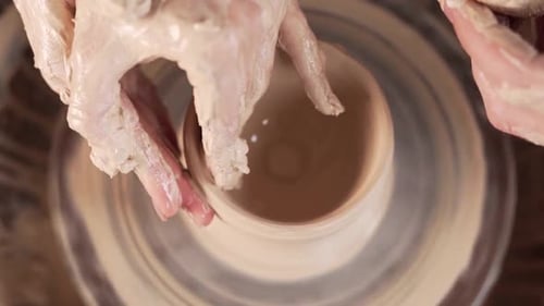 Closeup top view of female and male hands making pottery wheel