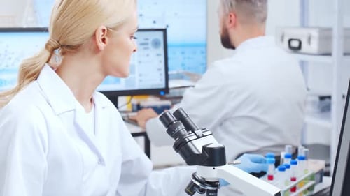 Scientist Studying Sample Through Microscope in Laboratory