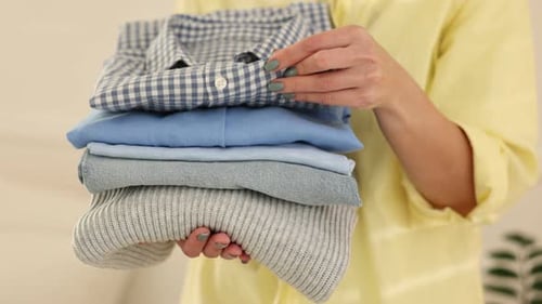 Woman with stack of clothes indoors, closeup. Camera moving in