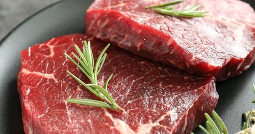 Raw beef steaks and rosemary on table, closeup