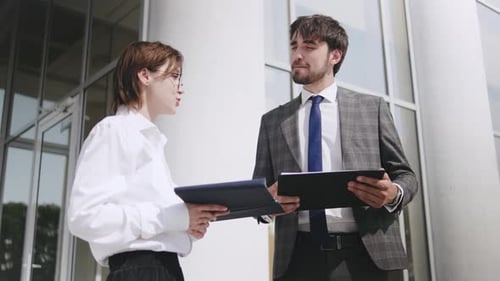 Business Meeting with Tablet Between Two Professionals Outside a Modern Office Building on a Sunny
