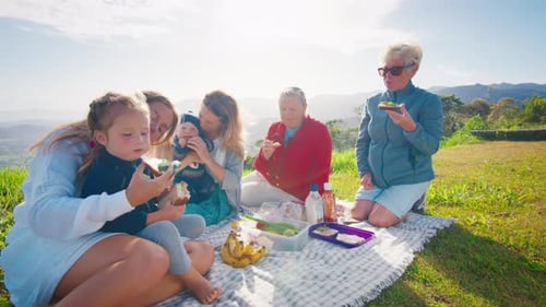 Big Family Have Picnic on the Green Hill in the Mountains at Sunrise