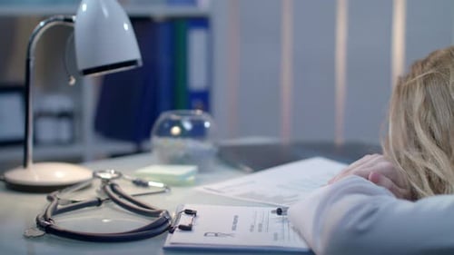 Exhausted Doctor with Head on Desk in Office