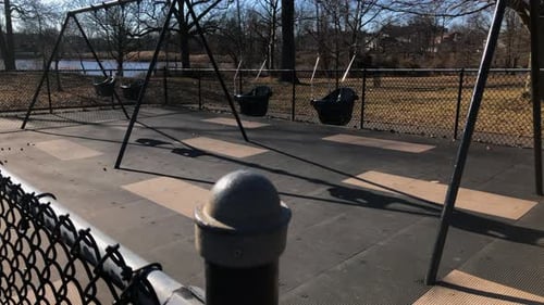 Leere Schaukel für Kleinkinder im Park, Winterzeit. Die Kamera schwenkt den Zaunpfosten hoch und zeigt die Schaukel
.
