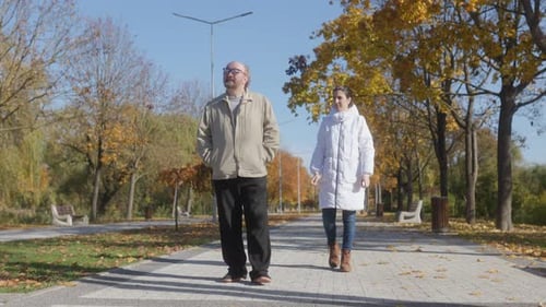 Senior Man with Supportive Caregiver on Calm Autumn Park Stroll