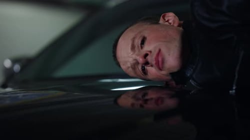 Man lying down on car with pained expression