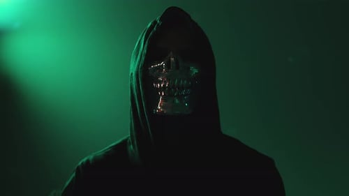 Hacker mascarado de pé com os braços cruzados de frente para a câmera na escuridão — conceito de ameaça à segurança cibernética