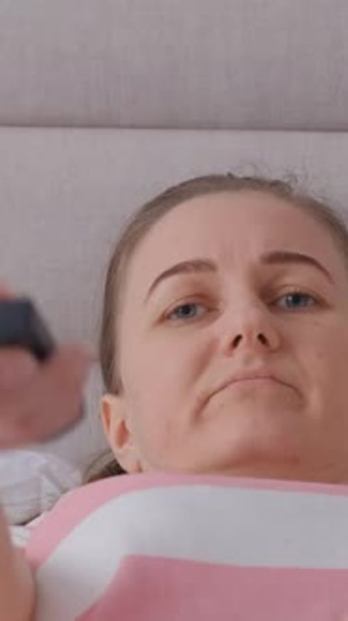 Bored Woman in Bed Holding a Remote Control