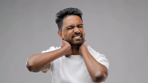 Unhealthy indian man suffering neck pain touching aching muscles on grey background
