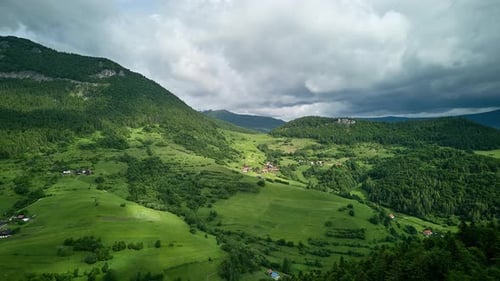 Aerial Hyperlapse Over Green Hills Forests and Rural Village Under Cloudy Sky
