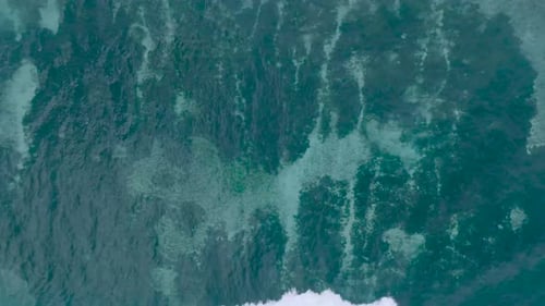 Top Down Slow Motion Drone View of crystal clear water and crashing waves over shallow coral reef in