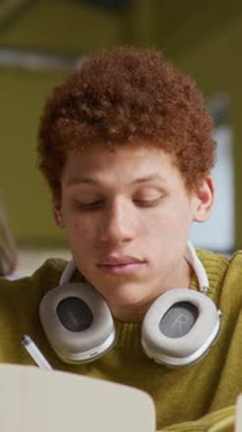 Male Student with Headphones Taking Notes during Lecture in College