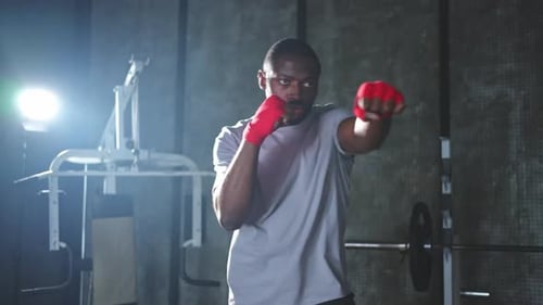Fitness Workout in Gym African Man Fighter Preparing for Fight Punching with Red Boxing Wraps Sports