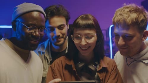 Gruppe verschiedener junger Leute, die sich auf einer Party Fotos auf dem Smartphone ansehen