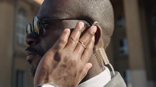 Black Male Security Agent Adjusting Earpiece Outdoors by Government Office
