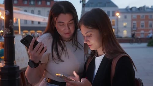 Two Women Using Smartphones in European City Square