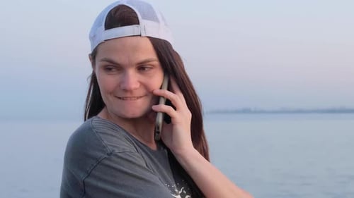 young woman talking using smartphone against sea background in evening