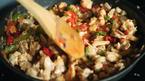 Nahaufnahme eines Holzlöffels, der die Zutaten für Hühnchen-Fajitas mischt und in einer Pfanne kocht.
