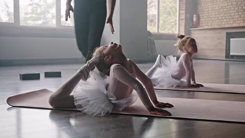 Little Girls Do Stretching on Mats Under Ballerina Control