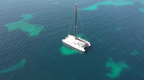 A Drone Flies Around a White Yacht with a Mast Standing in the Clearest Turquoise Sea