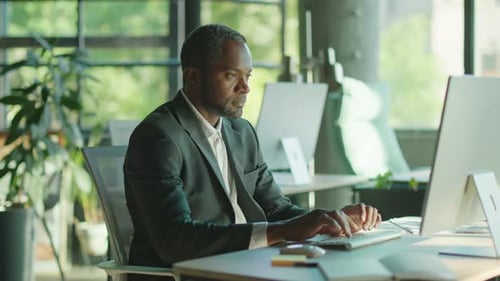 Im Light Office Attraktiver Afroamerikaner, der am Computer arbeitet und in eine Kamera schaut
