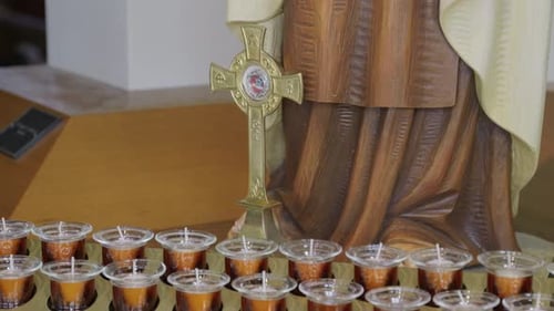Close-up panning shot of prayer offering candles, cross and statue
