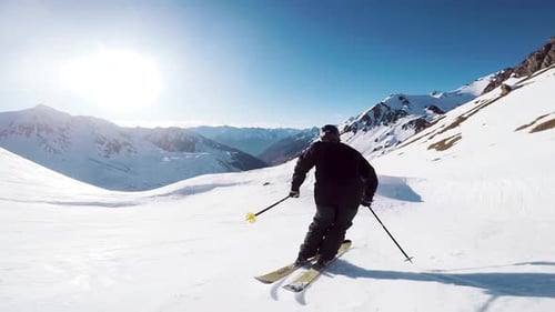 slow motion view of a skier dressed in black gracefully skiing in the mountains with beautiful sunli