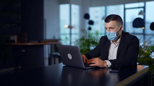 Man Working on Laptop With Mask in Office