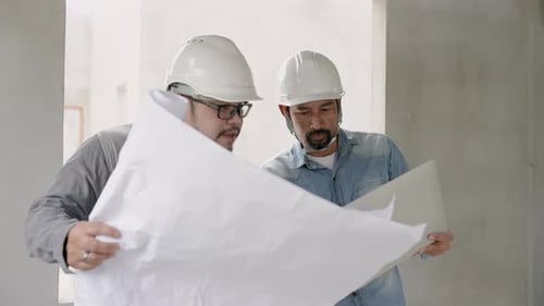 Bearded Indian engineer wearing helmet Stand and give orders to the foreman. Follow plan in blueprin