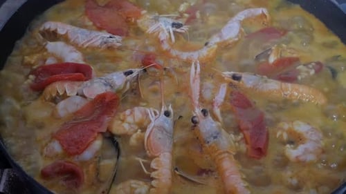 Paella boiling rice and ingredients being cooked on pan. Golden orange water from aromatic spices si