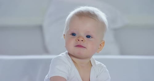 Ein Baby, ein Junge mit großen blauen Augen und hellen Haaren, sitzt und lächelt auf einer schneeweißen Decke