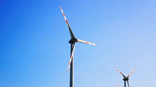 Wind turbines in blue skies. Two wind turbines with red and white blades stand tall against