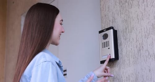 Woman pressing button on intercom panel outdoors
