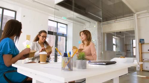Business Lunch And People Concept - Happy Businesswomen Eating Take Out Food At Office