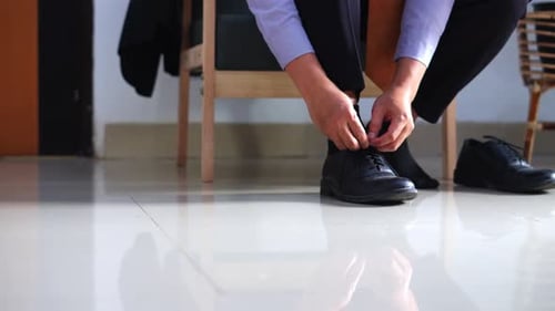 Man Ties Shoelaces on Shiny Black Leather Shoes