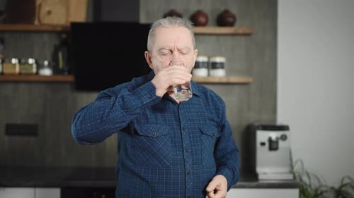 Mature Adult Takes Pill with Water in Kitchen