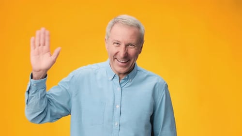 Man Waves Hand While Smiling Against Bright Orange Background in Footage