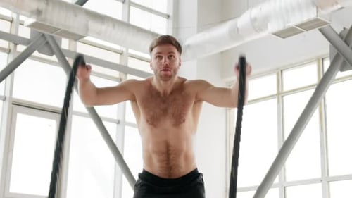 Slow Motion of a Young Caucasian Man Performing Battling Ropes Exercises in Gym