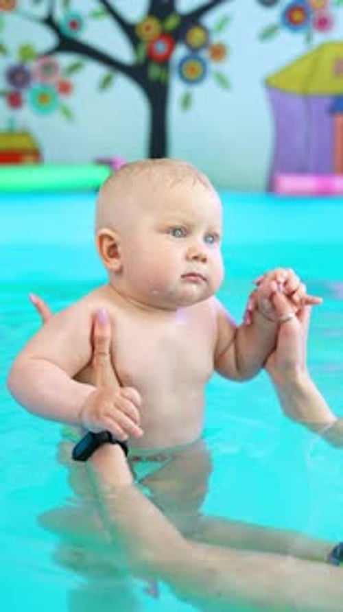 Female hands holding a little cute baby in the swimming pool. Lovely infant child learns to swim.