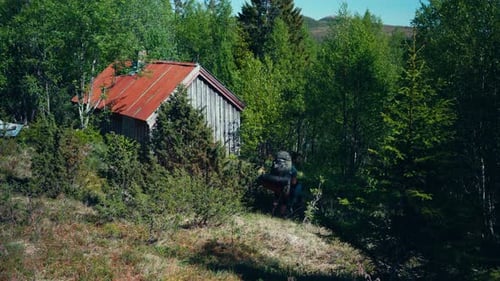 A Hiker and His Alaskan Malamute Pause For a Rest Close to a Quaint Chalet - Static Shot