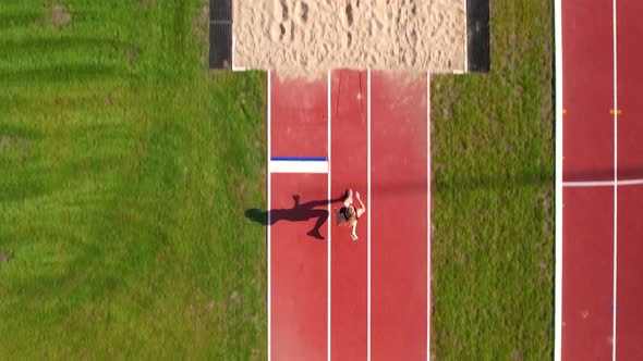 Aerial view of an athlete landing in a sandpit after a long jump, her ...