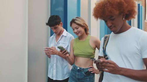 Three friends walking down the street holding mobile phones