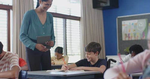 Assisting student with tablet in classroom, teacher engaging in school discussion