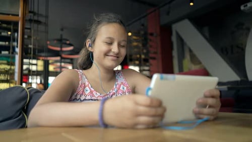 Teenage Girl Watching Movie On Tablet Computer Sitting In Cafe